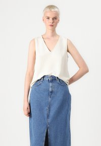 Top sans manches crème avec un décolleté en V, associé à une jupe en denim taille haute, arrivant au genou, avec une fente sur le devant.