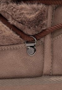 Bota con un forro de imitación de piel de fur que tiene textura, un exterior de cuero suave y un acento metálico cerca de un cordón marrón.