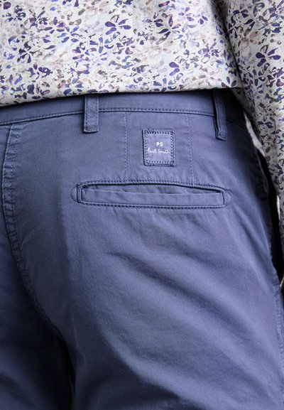 I pantaloni in cotone blu navy presentano una tasca posteriore con un'etichetta quadrata cucita con la scritta "PS Paul Smith". Il tessuto ha una consistenza liscia.