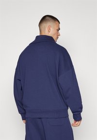 Sudadera de corte oversized en azul marino con un cuello alto, puños y dobladillo de canalé, hecha de un material suave; presenta un ajuste relajado y hombros caídos.