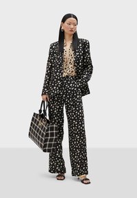 Crni i bež odijelo s točkicama s širokim hlačama i sakoom. Upareno s torbom koja ima sličan uzorak i crnim sandalama. Glatka tekstura.