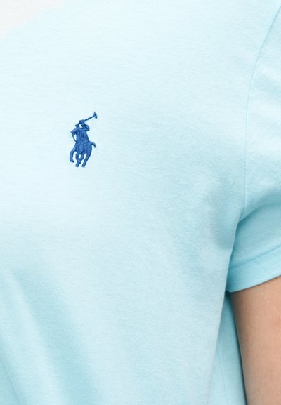 Gaiši zils kokvilnas T-krekls ar zilu izšūtu polo spēlētāja logotipu uz kreisās krūtis. Īsas piedurknes un klasisks apaļš kakla izgriezums.