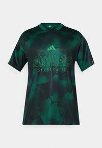 Zelené tričko Adidas se vzorem kamufláže, vyrobené z texturované látky, s kulatým výstřihem a s kontrastním logem v tučném písmu.