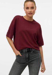 T-shirt bordeaux a maniche corte con scollatura rotonda abbinato a jeans grigi scuri a vita alta, caratterizzati da una texture liscia e una vestibilità casual.