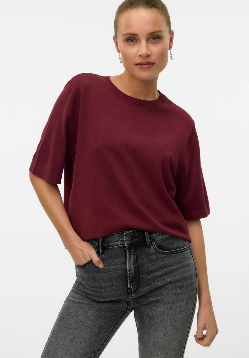 T-shirt bordeaux a maniche corte con scollatura rotonda abbinato a jeans grigi scuri a vita alta, caratterizzati da una texture liscia e una vestibilità casual.