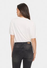 Vit kortärmad topp i kombination med högmidjade mörka jeans som har en läderpatch och diskret fickstoppning. Enkel, figursydd design.