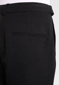Pantalon noir en tissu texturé avec une coupe slim, doté d'une poche arrière unique et d'un design sobre et épuré.