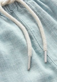 Svetlé modré látkové materiály s texturovaným vzorem; má bílou šnůrku s kovovými konci a stažený pas.