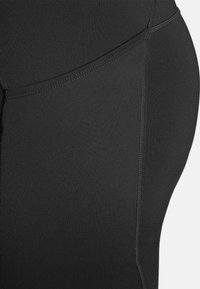 Leggings de sport noirs avec une texture lisse, un design ajusté et des coutures plates. Le tissu a une finition mate sans motifs visibles.