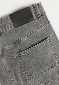 Szare dżinsy z denimu z czarną skórzaną metką z wytłoczonym logo, tylną kieszenią i widocznymi detalami szwów wzdłuż szwów.