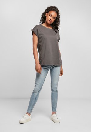 Grå t-skjorte med korte ermer og avslappet passform, kombinert med lyseblå skinny jeans og hvite joggesko. Glatt stoff og enkel design.