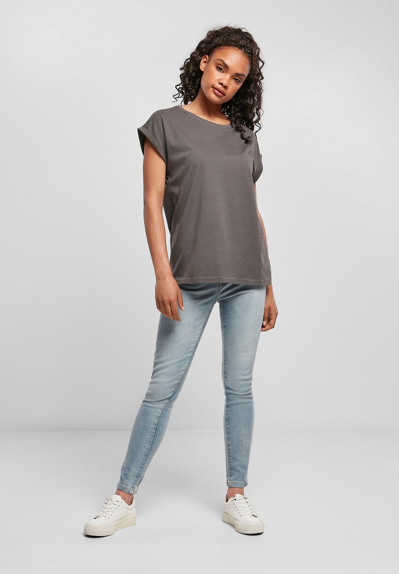 T-shirt gris à manches courtes de coupe décontractée, associé à un jean skinny bleu clair et des baskets blanches. Tissu lisse et design simple.
