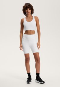 Un sutien sport alb și pantaloni scurți de ciclism cu talie înaltă, asortați, dintr-un material neted și elastic. Tenisi cu accente negre completează ținuta.