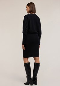 Abito nero lavorato a maglia con maniche lunghe e silhouette aderente, abbinato a stivali neri alti fino al ginocchio con stampa cocodrillo.