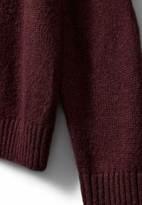 Burgundy knitted sweater featuring a textured fabric, ribbed cuffs, and a slightly loose fit. Close-up view emphasizing material details.