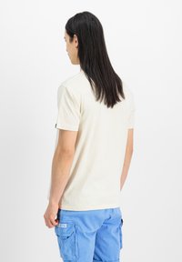 Cremefarvet kortærmet t-shirt med rund hals, lavet af blød bomuld, med et mærke på venstre ærme. Bæret med blå cargo-shorts.