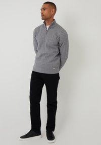 Šedá mikina na zip s texturovaným vzorem, v kombinaci s černými kalhotami a černými teniskami. Jednoduchý design s límečkem na čtvrtinu zipu.