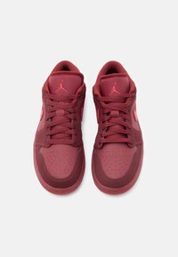 Κόκκινα αθλητικά παπούτσια με συνθετικό επάνω μέρος, στρογγυλεμένη μύτη, διάτρητες λεπτομέρειες και κορδόνια, με λογότυπο στη γλώσσα και στις πλευρές.