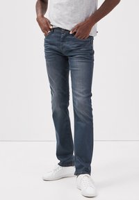 Ciemnoniebieskie dżinsy o slim fit, z średnim stanem, ukośnymi przednimi kieszeniami oraz subtelnym przetarciem. Zestawione z białymi sneakerami.