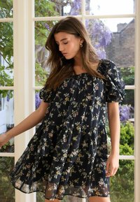 Svart blommig klänning med puffsleeves, flerårig design och genomskinligt tyg. Har små, flerfärgade blommor mot en mörk bakgrund.