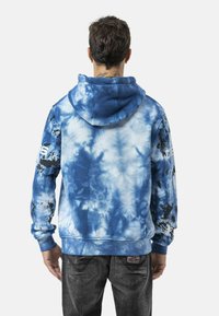 Blauwe tie-dye hoodie met verschillende tinten en patronen, voorzien van een buidelzak en geribbelde manchetten, getoond vanaf de achterkant.