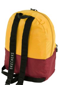 Mochila con parte superior amarilla y parte inferior marrón. Presenta correas ajustables negras y un cierre de cremallera. Logo "SKECHERS" en el lado.