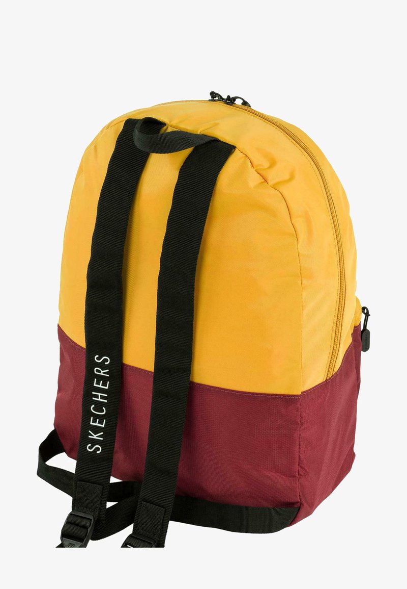 Mochila con parte superior amarilla y parte inferior marrón. Presenta correas ajustables negras y un cierre de cremallera. Logo "SKECHERS" en el lado.