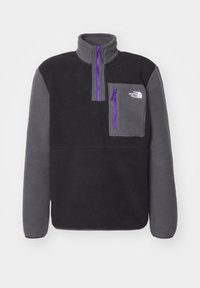 Sort og grå fleece pullover med lilla lynlåse, brystlomme og "The North Face" logo på øverste venstre bryst.