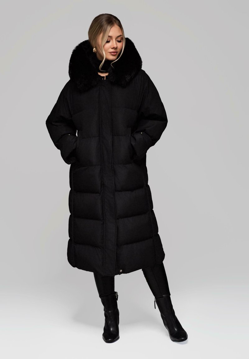 Cappotto puffa nero con colletto in pelliccia sintetica, maniche lunghe, tasche laterali e design trapuntato. Lunghezza al ginocchio con una vestibilità dritta e comoda.