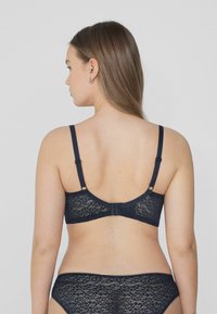 Bralette de encaje azul marino con tirantes ajustables y cierre de gancho. Presenta un patrón floral y delicados bordes festoneados.