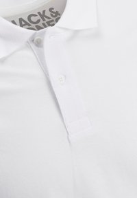 Chemise polo blanche en tissu texturé, dotée d'une patte de boutonnage à trois boutons et d'un col plat. Marque visible dans l'encolure.