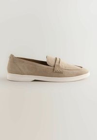 Mocassin beige en daim avec détail de bride et semelle en caoutchouc blanche, talon bas, style à enfiler, design minimaliste sur un fond clair uni.