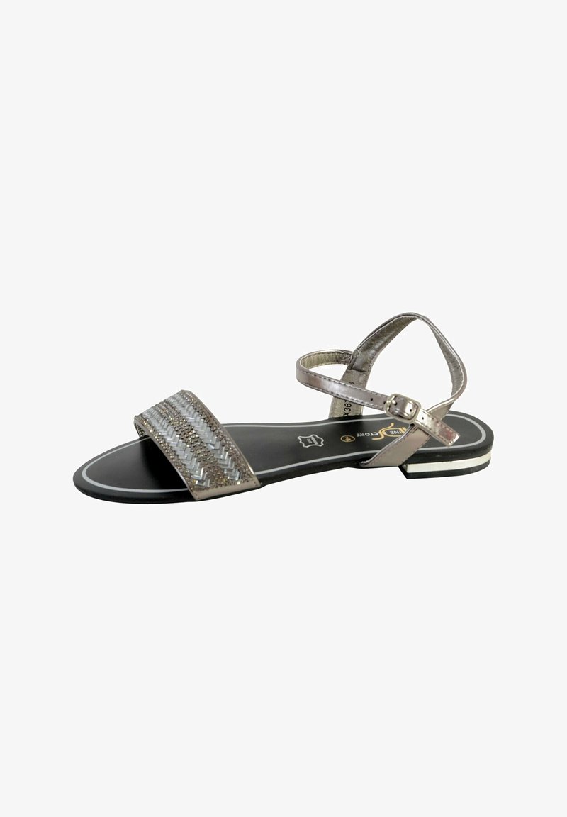 Flat sandals with a metallic silver strap design, woven texture on the front, adjustable ankle strap, and a black sole with white accents.