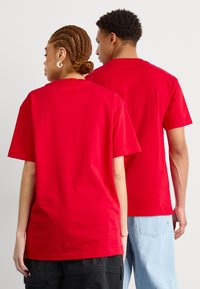 T-shirts en coton rouge à manches courtes et col rond. Le tissu semble lisse, avec une coupe décontractée. L'arrière-plan est blanc uni.