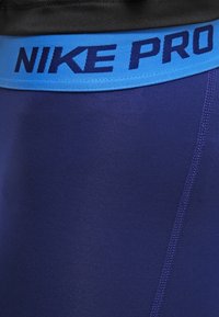 Námořnické modré sportovní šortky s modrým elastickým páskem s nápisem "NIKE PRO" v tmavě modré barvě. Hladká textura a úzký střih.