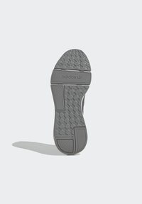 Gray Adidas shoe sole with patterned tread, textured grip areas, and Adidas logo on the midfoot, casting a shadow on a light background.