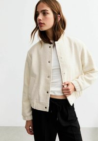 Crème-kleurige bomberjack van een textuur fleece materiaal, met drukknopen, zijzakken, gedragen over een slim-fit witte top.