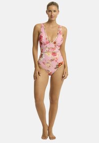 Różowy jednoczęściowy kostium kąpielowy z głębokim dekoltem w kształcie V, szerokimi ramiączkami oraz ozdobnymi poziomymi pasami; charakteryzuje się mieszanką dużych i małych wzorów kwiatowych.