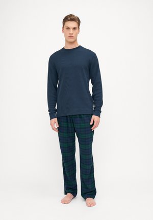 Haut thermique à manches longues bleu marine en tissu texturé, associé à un pantalon en flanelle à carreaux verts et bleus, avec une coupe décontractée et une taille élastique.