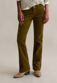 Olijfgroene corduroy flarebroeken met textuurstof, riemlussen, voorzakken en een enkele knoopsluiting, gecombineerd met beige enkellaarsjes.