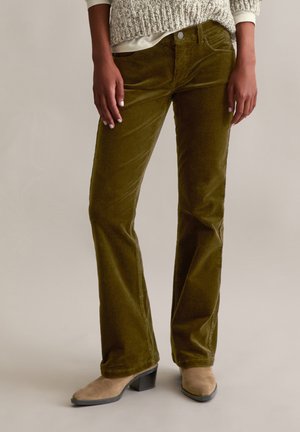 Olijfgroene corduroy flarebroeken met textuurstof, riemlussen, voorzakken en een enkele knoopsluiting, gecombineerd met beige enkellaarsjes.
