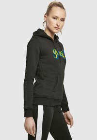 Sudadera negra con un bolsillo frontal, que presenta un diseño gráfico colorido en azul y amarillo. Material suave con puños y dobladillo acanalados.