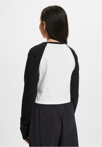 Long-sleeve raglan top featuring a white body and black sleeves, made of soft cotton. Cropped design with a rounded neckline and stitched seams.