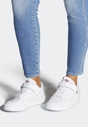 Hvide Adidas-sneakers med velcrolukninger båret med lyseblå skinny jeans på en lys baggrund.