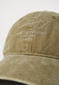 Khakifarbene Baumwollmütze mit gebogenem Schirm, die ein hellfarbenes gesticktes Logo und Text auf der Vorderseite zeigt, sowie sichtbare, strukturierte Stoffdetails.