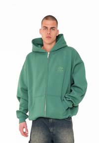 Grüne Zip-Hoodie aus Sweatshirt-Material. Verfügt über eine große Kapuze, frontale Taschen und ein kleines geprägtes Logo auf der linken Brust.