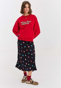 Červená mikina s textem "mucho amor", doplněná černou sukní s barevnými vzory srdcí. Doplňky zahrnují boty s leopardím potiskem.