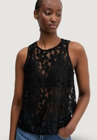 Top senza maniche nero con design in pizzo floreale, tessuto trasparente, scollatura rotonda e vestibilità comoda. Indossato con jeans blu.