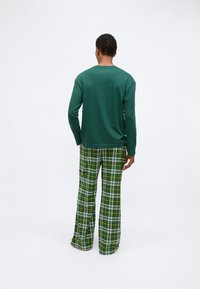 Πράσινο πουκάμισο με μακριά μανίκια σε συνδυασμό με καρό παντελόνι που διαθέτει χρώματα πράσινο, λευκό και κίτρινο. Και τα δύο έχουν χαλαρή εφαρμογή και είναι κατασκευασμένα από υφαντό ύφασμα.