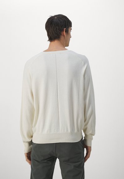 Pulover tricotat de culoare crem, cu mâneci lungi, cu manșete și margine cu textura ribbed, având un design simplist și detalii de cusătură pe spate.